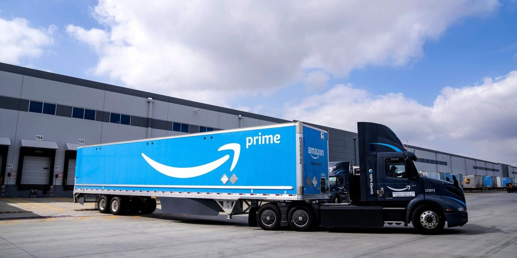 An electric Amazon semi-truck with a blue Prime trailer is parked in a logistics lot.
