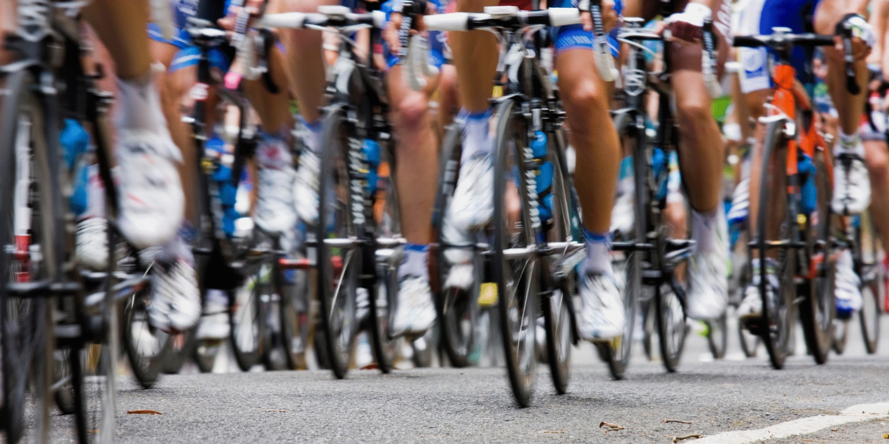 A large group of cyclists in a professional race, focusing on the wheels and legs of the riders as they speed along an asphalt road.