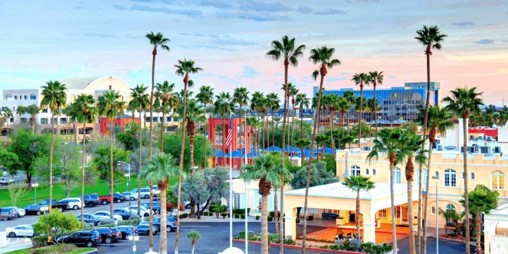 Sunny resort landscape with tall palm trees, a parking lot, and corporate buildings under a sunset sky.