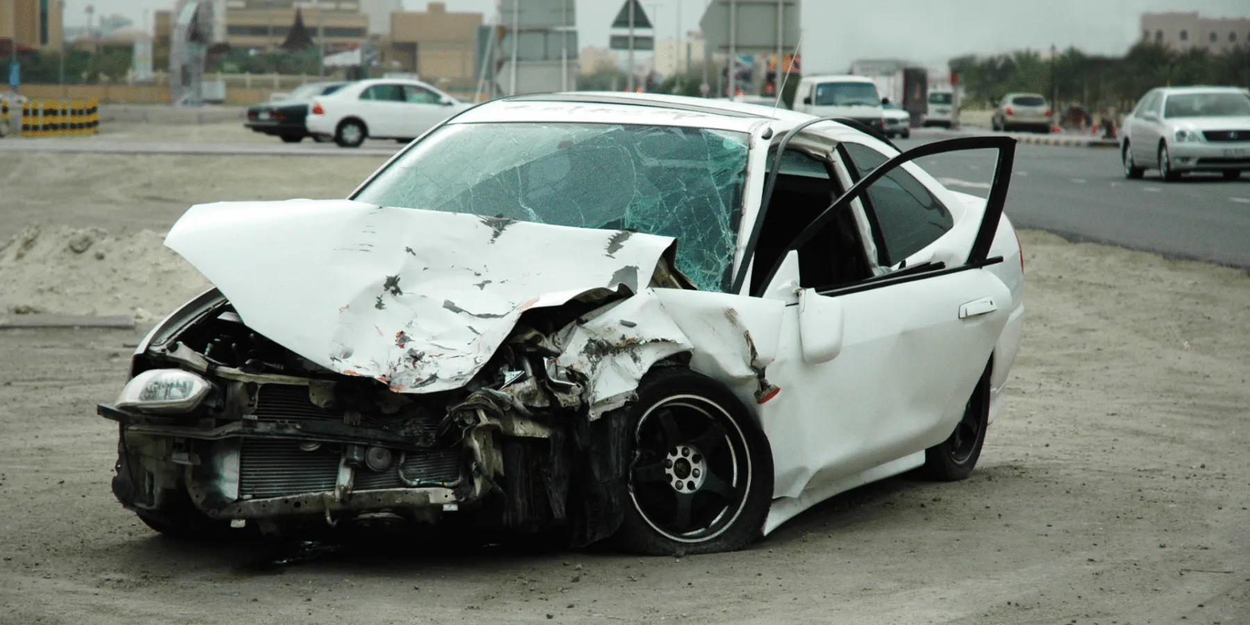 A heavily damaged white sedan with severe front-end impact and a shattered windshield.
