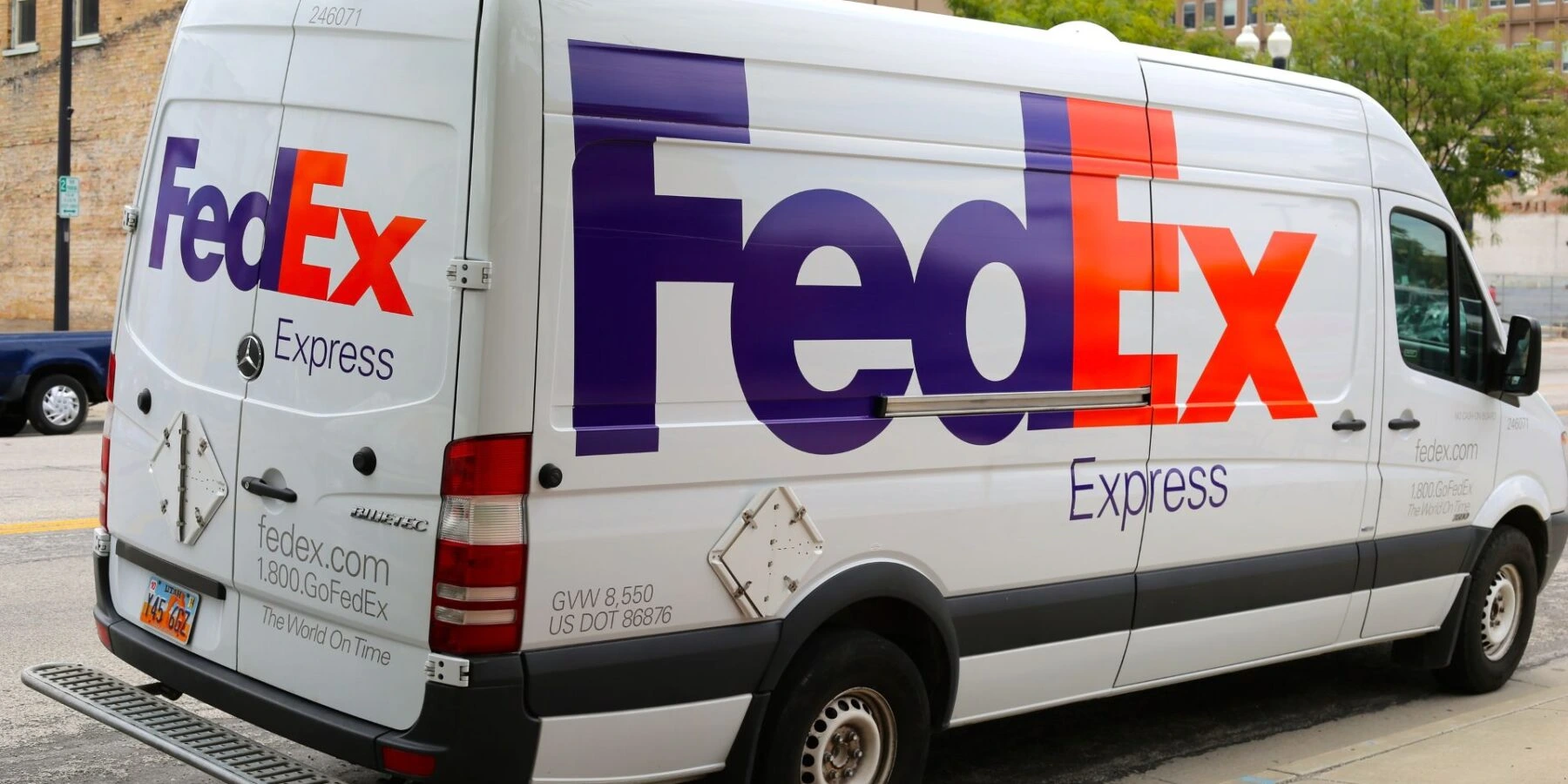 A white FedEx Express delivery van is parked along a city street during the day.