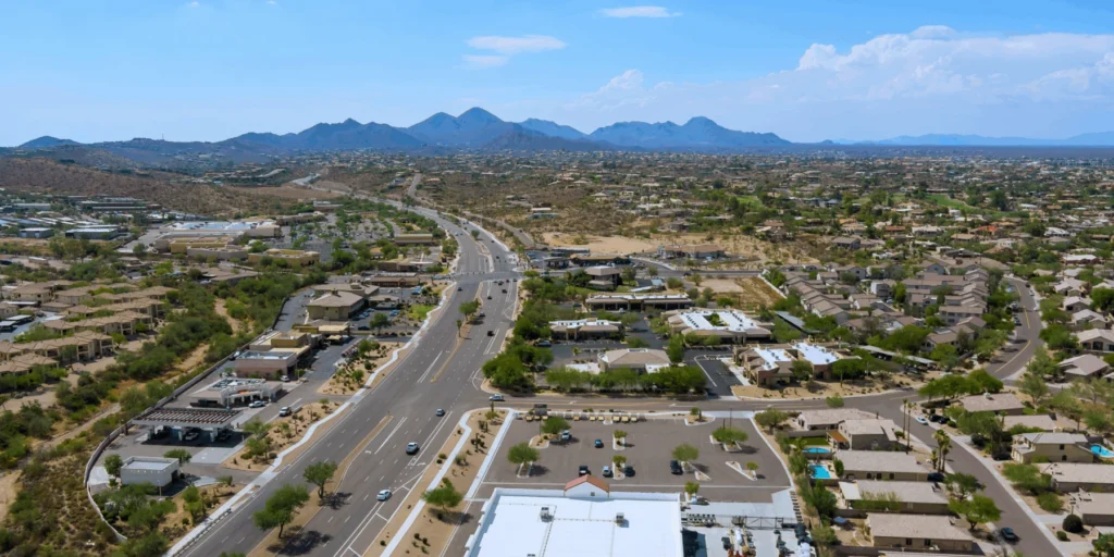 A desert city suburb with a multi-lane road, residential neighborhoods, and mountains in the distance.