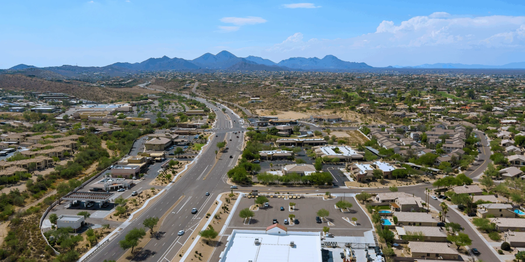 A desert city suburb with a multi-lane road, residential neighborhoods, and mountains in the distance.