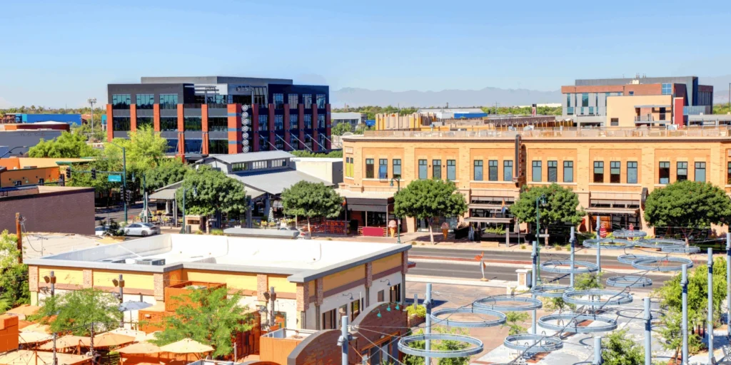 Sunny downtown street with modern buildings, retail patios, and trees.
