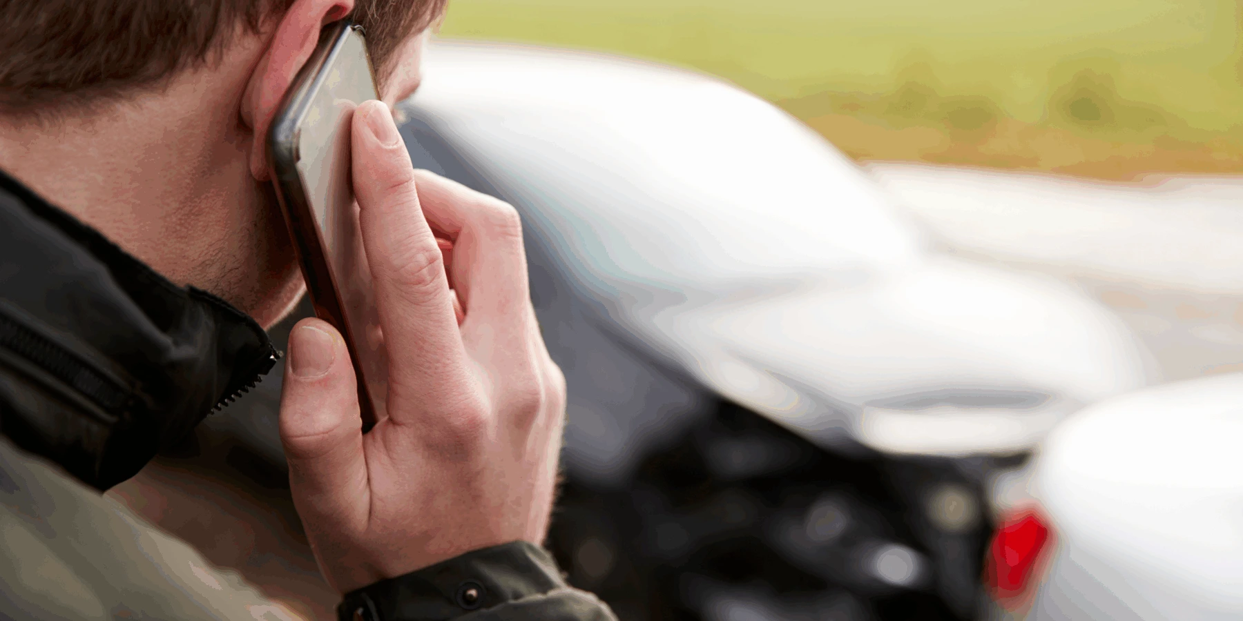 A man speaking on a smartphone with a blurred car accident in the background.