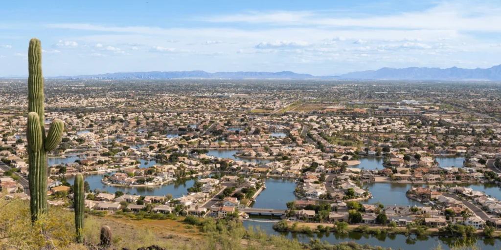 A desert suburb featuring waterfront homes, a large lake network, and tall saguaro cacti in the foreground.