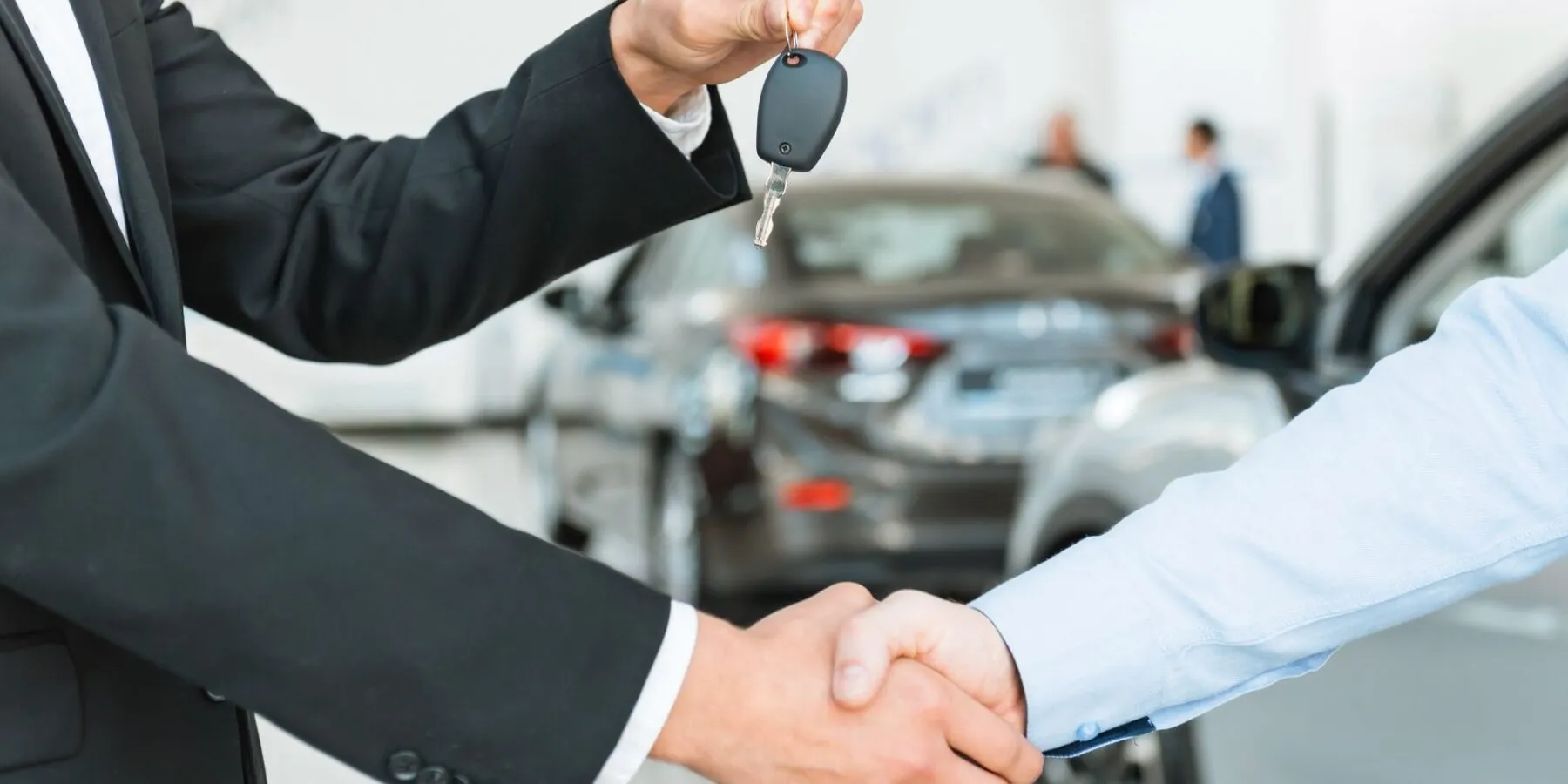 Two people in business attire shaking hands in front of a blurred car