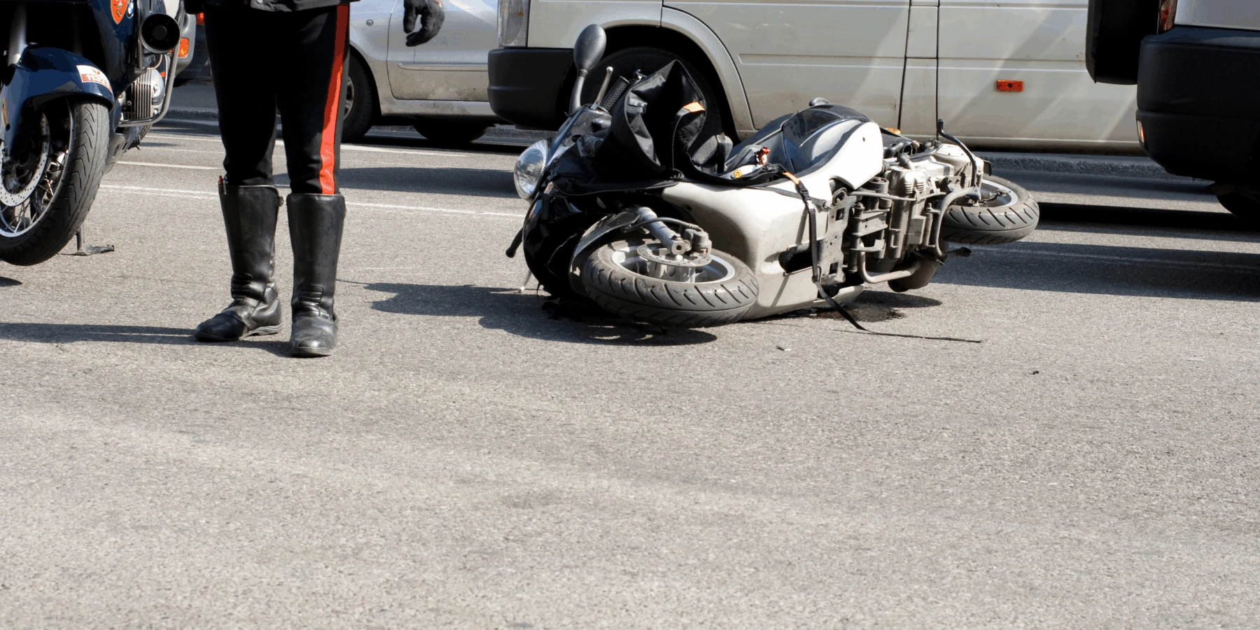 A motor scooter lying on its side on a city street at the scene of an accident, with a first responder standing nearby.