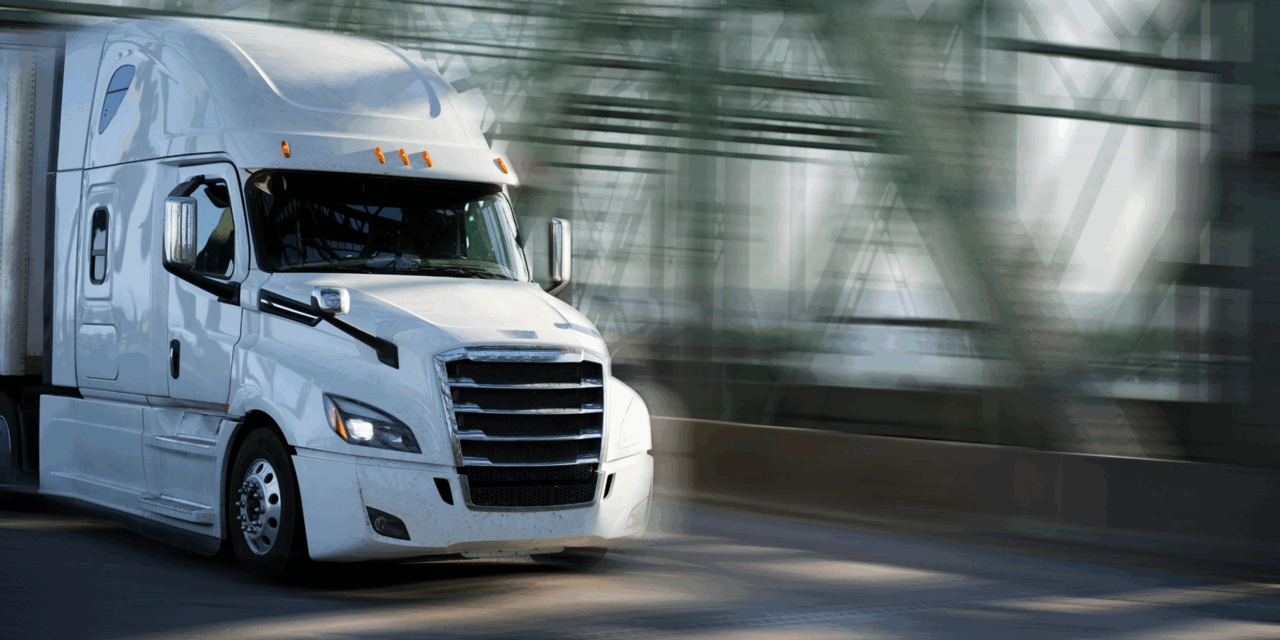 A white semi-truck driving across a bridge with a motion-blurred green steel structure in the background.