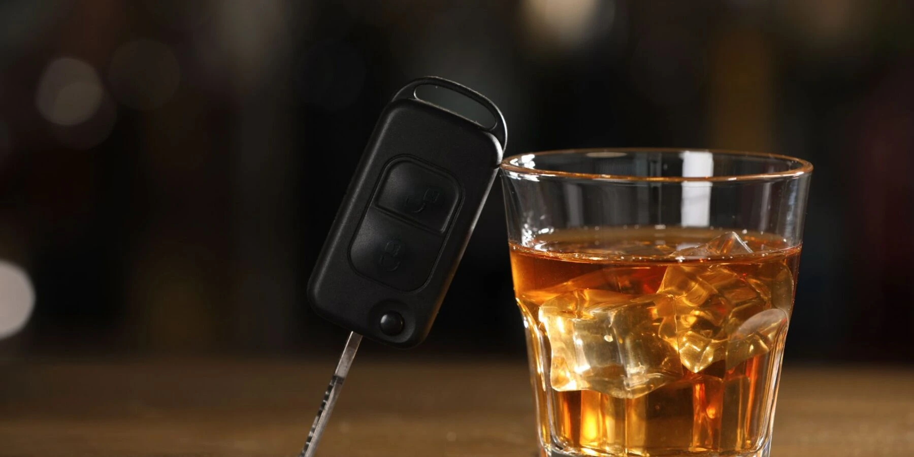 A car key fob leaning against a glass of amber liquid with ice.
