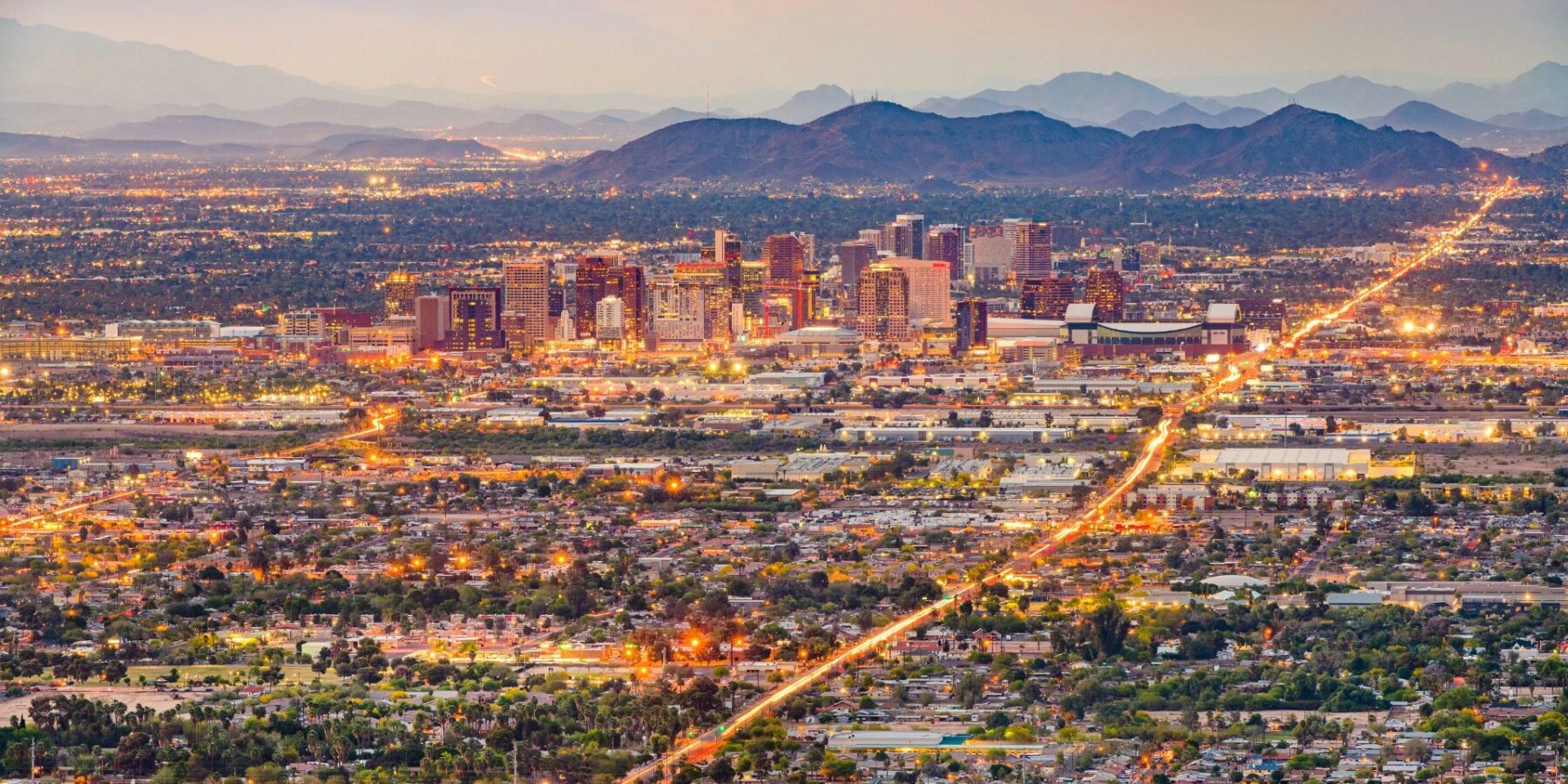 A skyline at twilight with a backdrop of rugged mountains and glowing city lights.