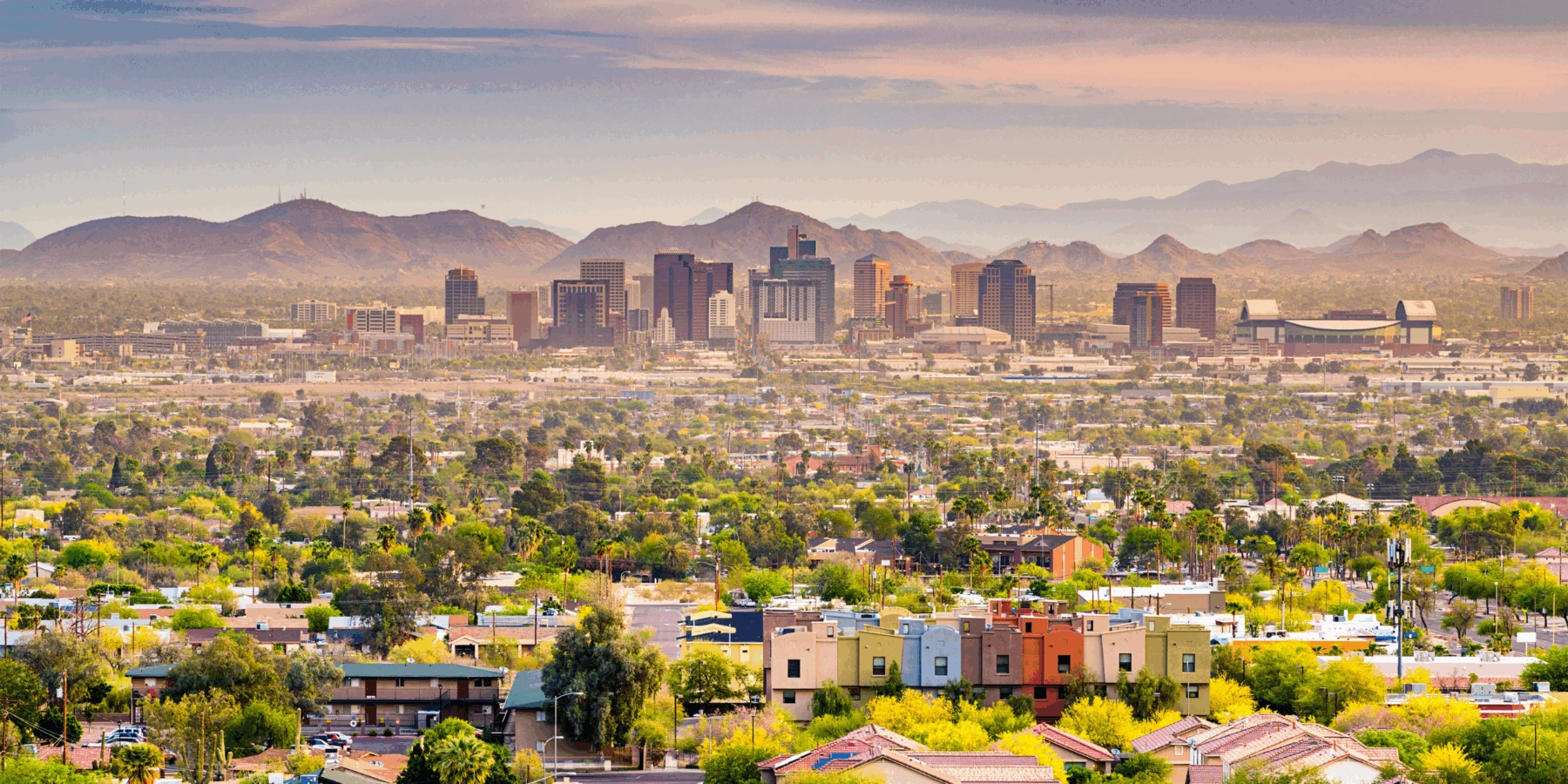 Daytime view of the Phoenix skyline and urban landscape set against desert mountains under a hazy sky.