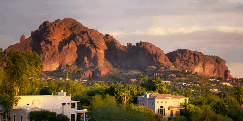 A scenic panoramic view of Camelback Mountain in Arizona, glowing with warm orange and red hues under a partly cloudy sky.