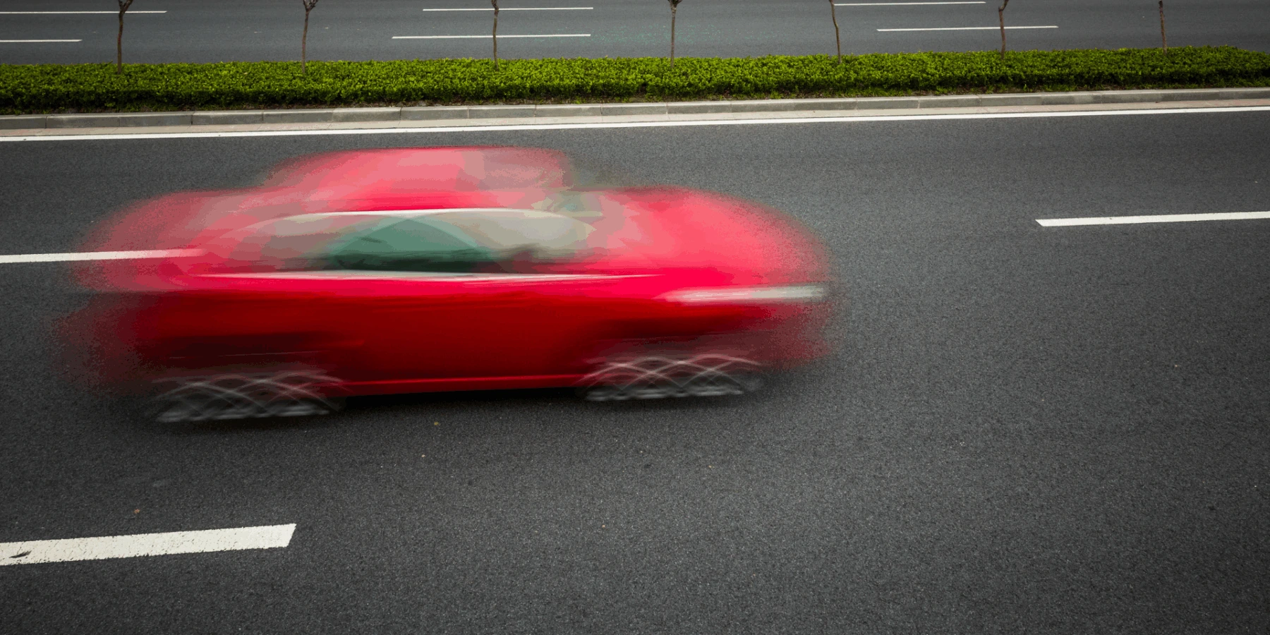Blurred red car speeding on a multi-lane road.