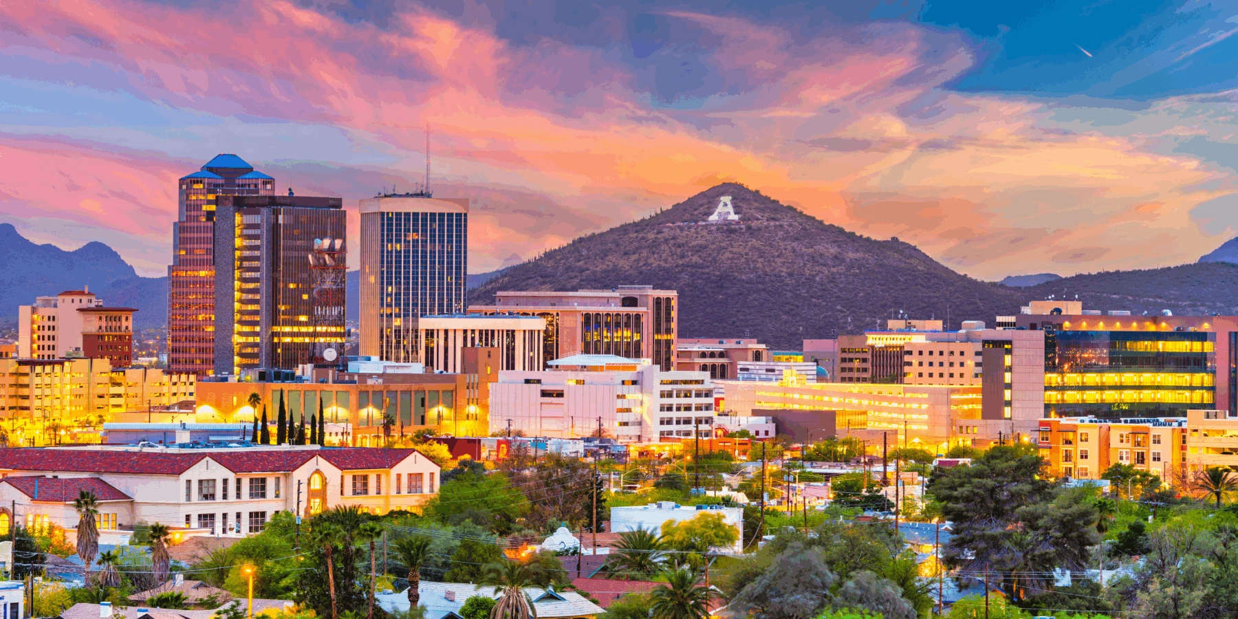 A vibrant sunset view of the Tucson, Arizona skyline featuring illuminated city buildings and a Mountain.