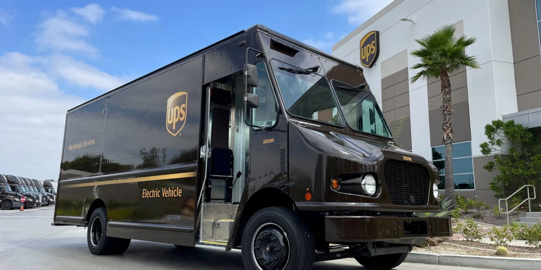 A brown UPS delivery truck with "Electric Vehicle" printed on its side is parked in a lot.