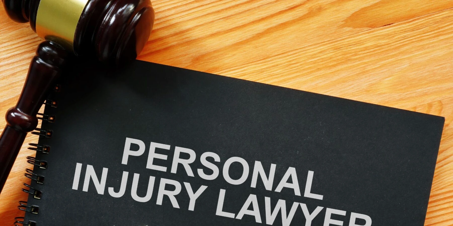 A wooden gavel rests on a black notebook that has the words "PERSONAL INJURY" printed on it.